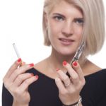 Close up Young Blond Woman in Black Clothing Holding a Tobacco and E-Cigarette on a White Background.