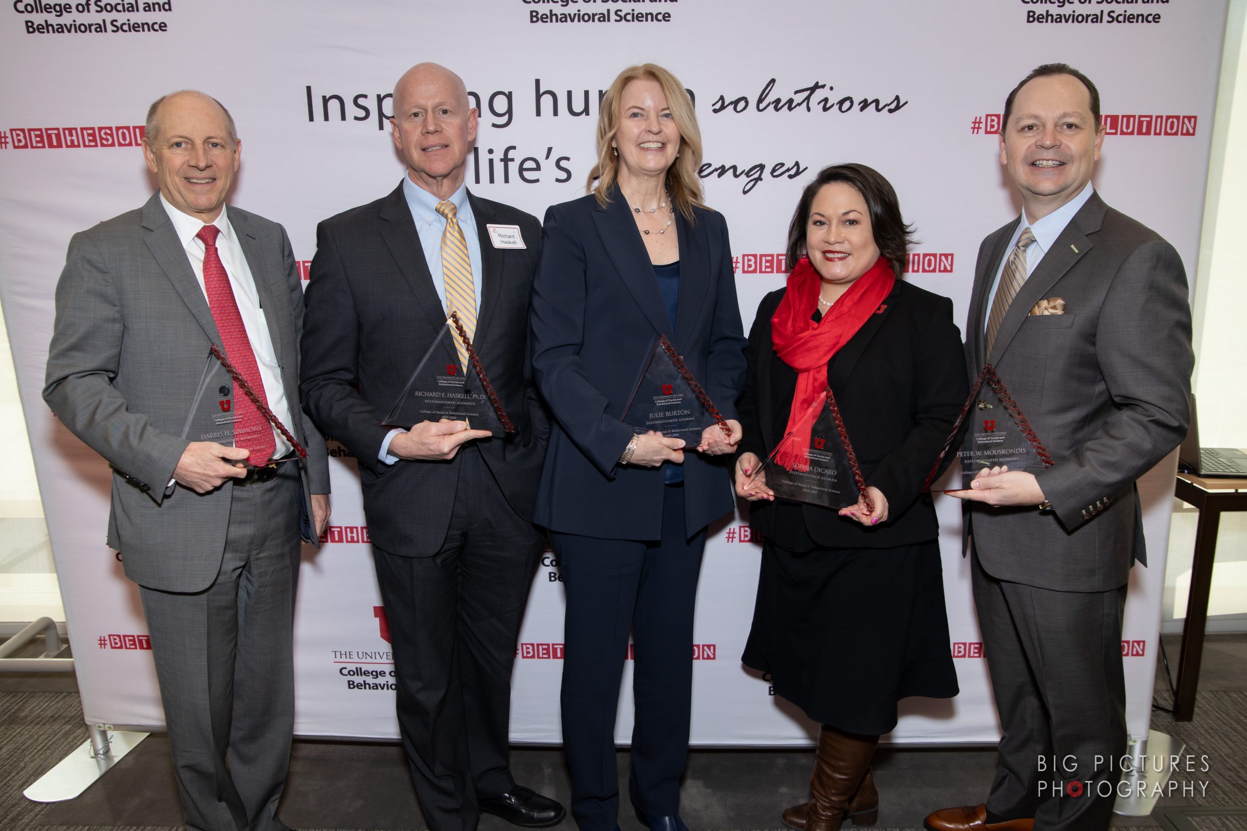 Three men and two women stand against a backdrop holding clear glass awards.