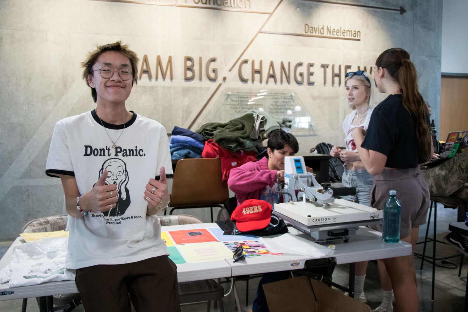 A student wears a camera and smiles. "Don't panic" A T-shirt with clothes on the back of the table.