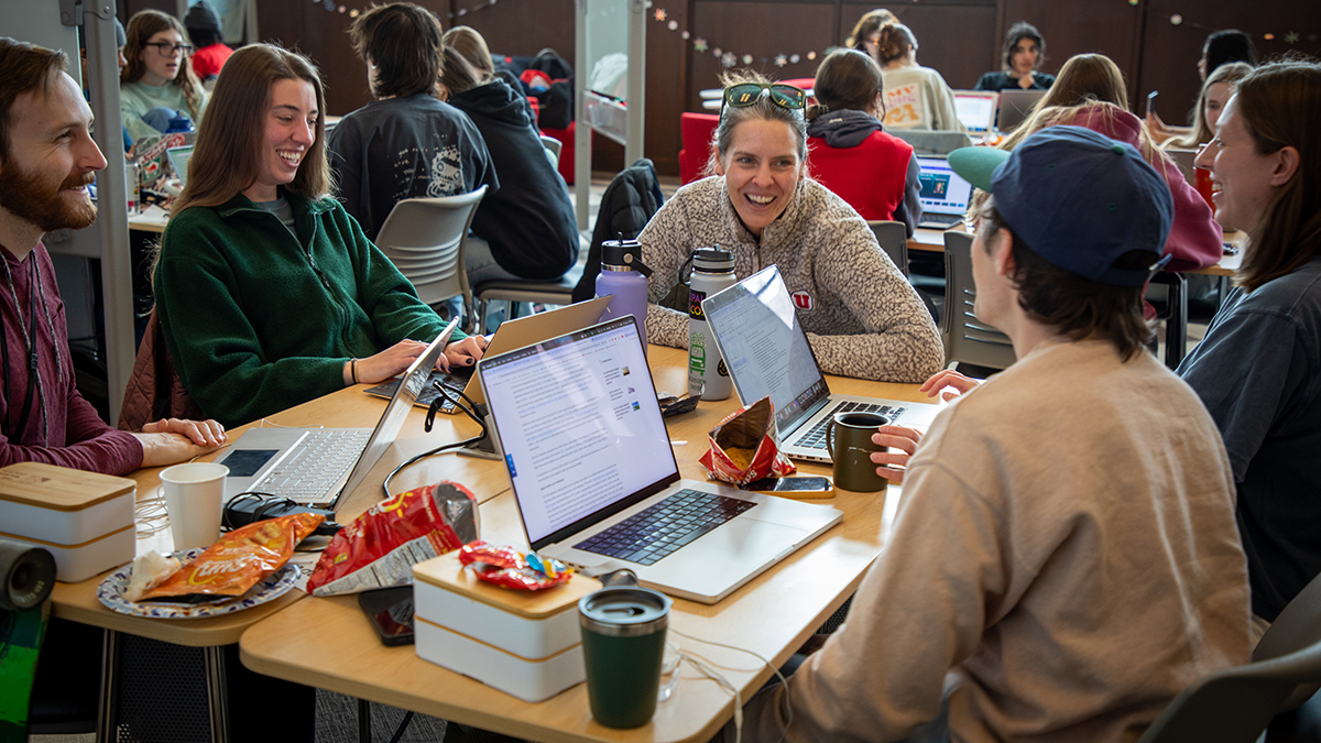 A group of students laugh around a large table, with laptops open and thoughts-a-flowin'.