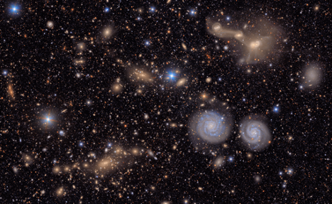 An image of space with a black background with spiral galaxies and distant yellow glowing specks.