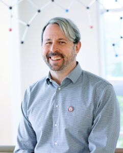 Headshot of man in a gray button up shirt.