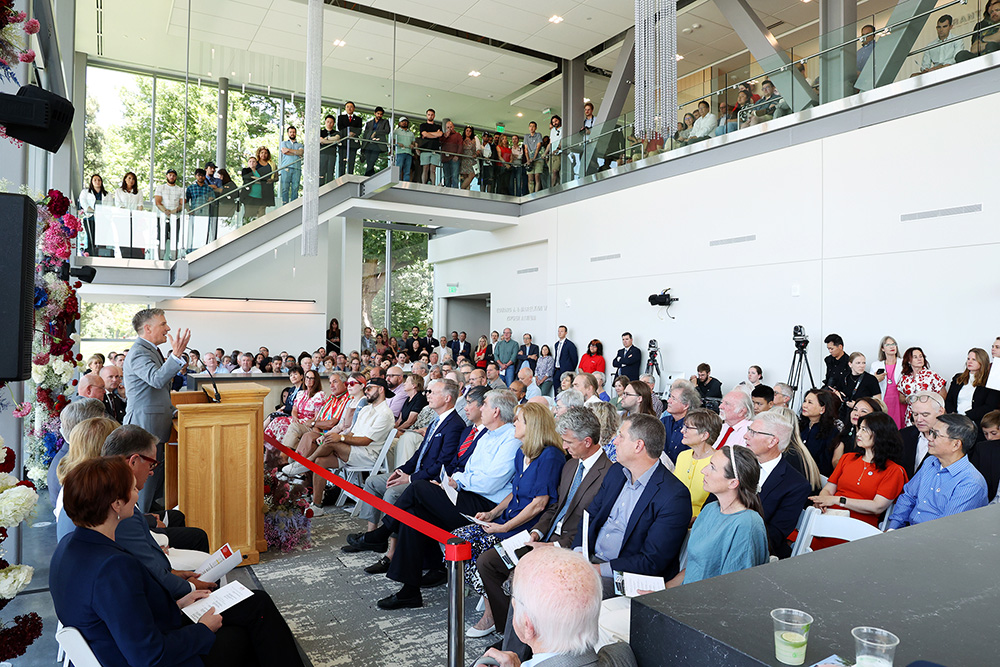 A man speaks at a podium to a packed atrium.