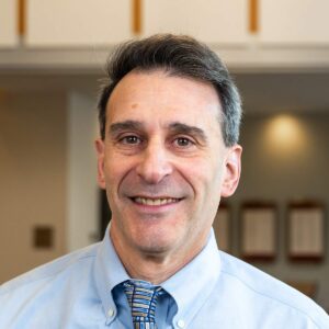 Headshot of a man with a light blue shirt and patterned blue tie.