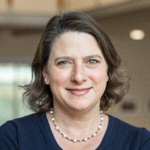 Headshot of a woman with a black top and necklace.