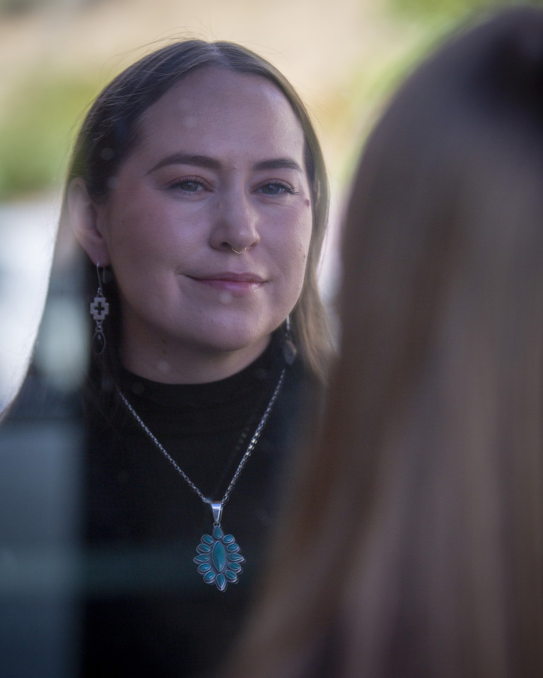 A woman in a black mock turtleneck, wearing a silver necklace with turquoise stones and silver earrings with a Navajo cross and a dark oval stone.