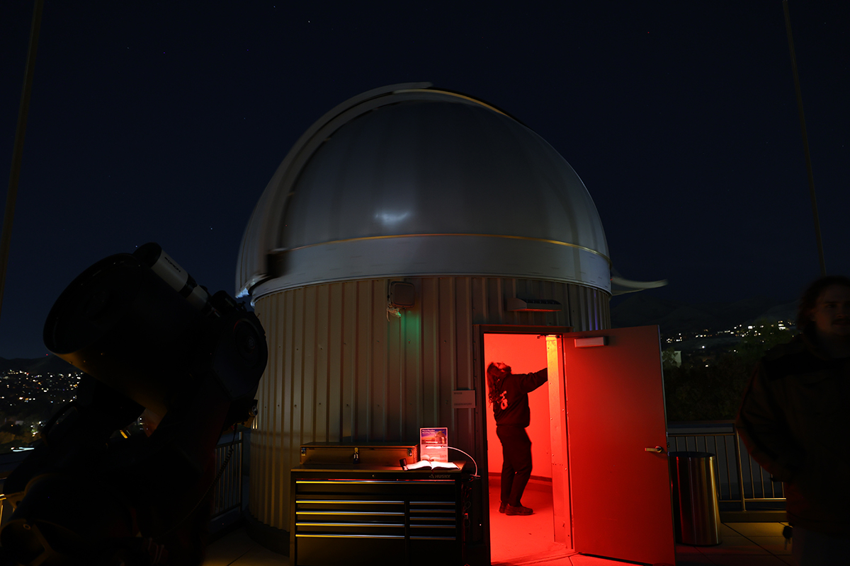 A crowd looks through multiple telescopes on a roof.