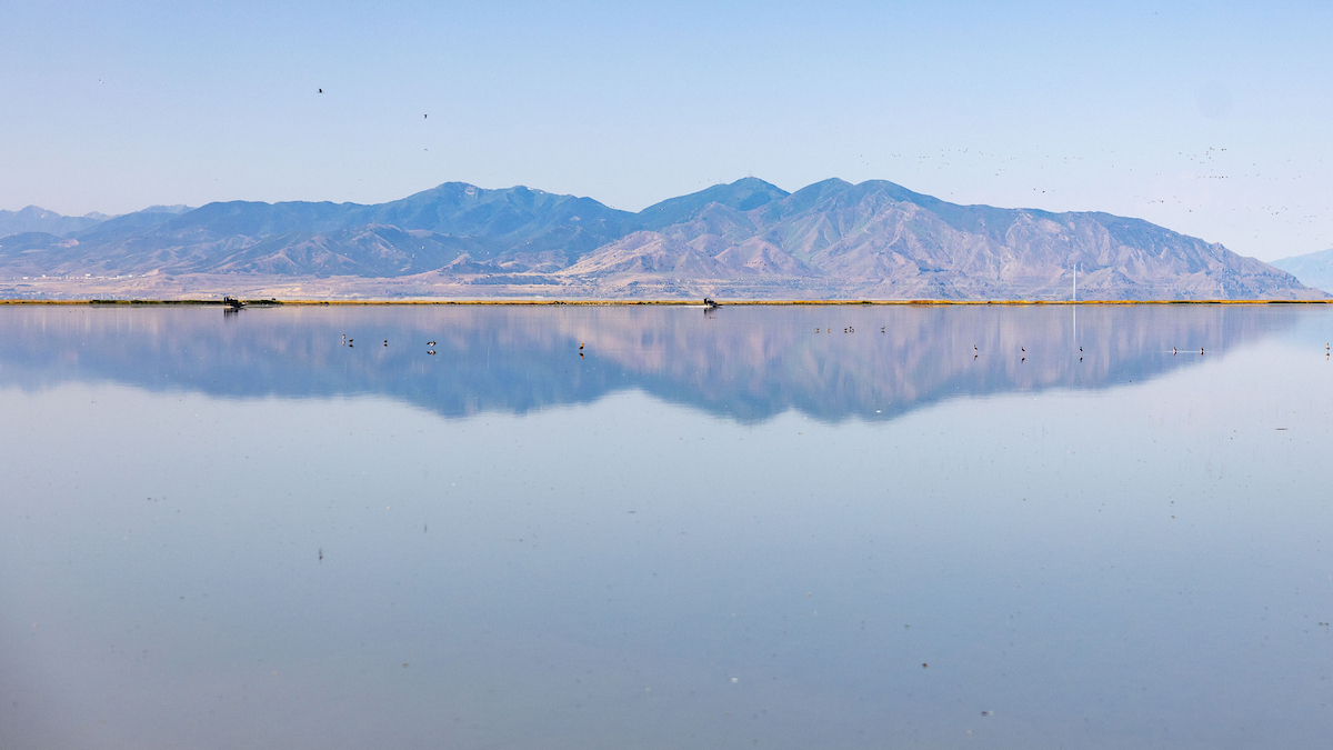 A landscape photo of the Great Salt Lake with a landform perfectly reflected in the water.