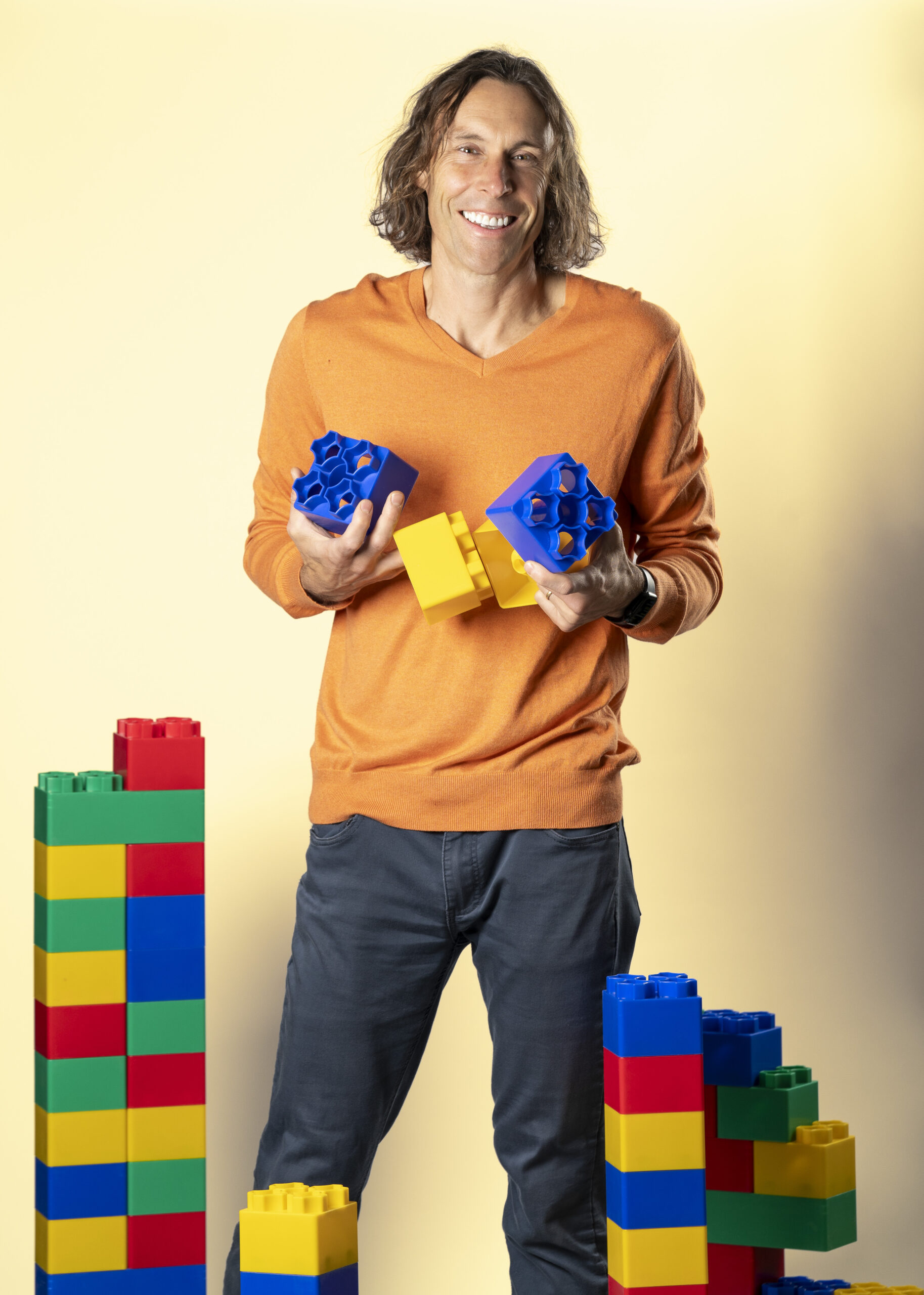 A man holds giant legos behind towers of legos.