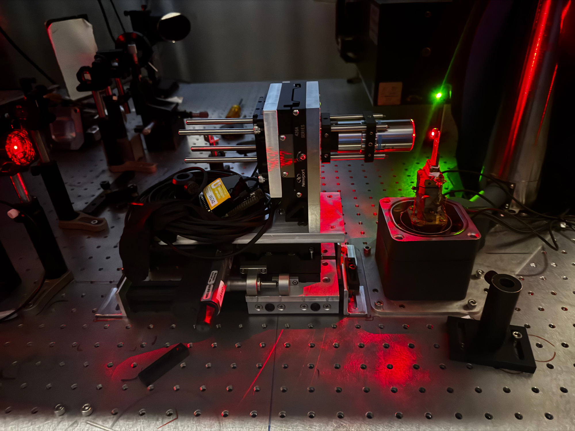 Photo of physics lab equipment. A complicated set up of different metal rods, with green and red light shooting out of some of them.