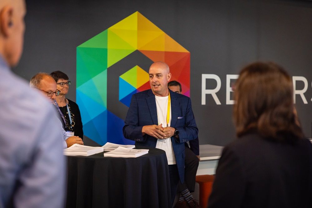 A man stands in front of a rainbow, prismatic geometric Recursion logo.