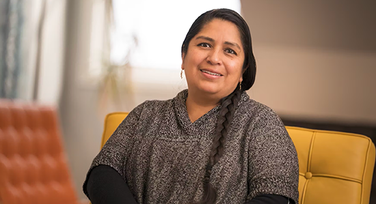 Smiling woman with dark hair sitting on a yellow armchair.