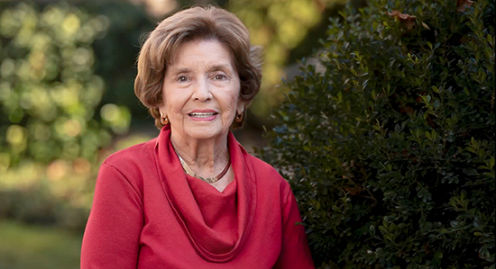 Senior woman in a red cowl-neck sweater sitting in a garden.