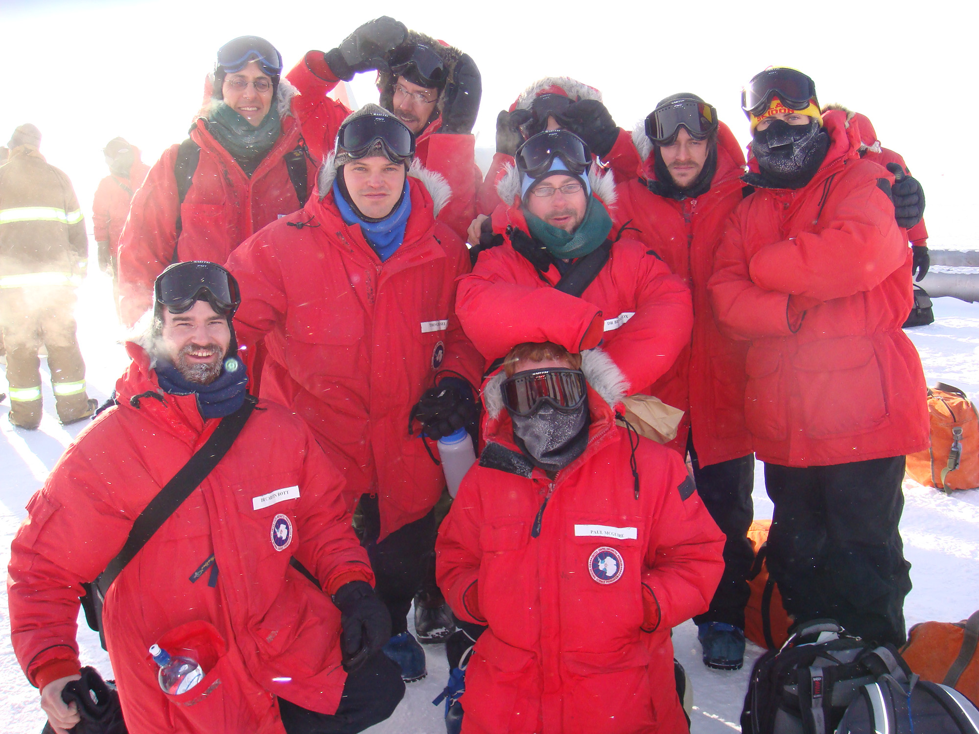 A group of researchers wearing red parkas with fur hoods in Antarctica.