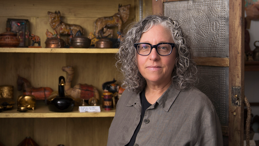 A woman standing beside a display cabinet filled with antique objects.