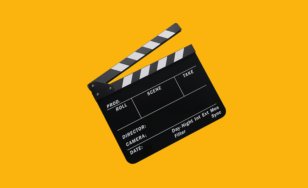Black film clapperboard with labeled fields for production, scene, and take on a yellow background.