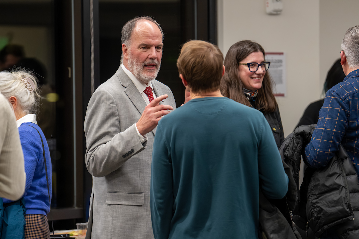 A man in a gray suit talk s to a young man with his back to the camera.
